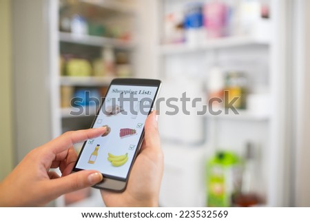 Woman makes her shopping list on his phone connected to the refrigerator