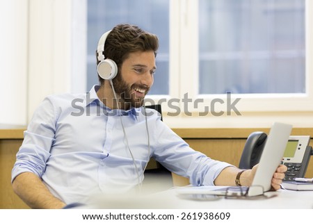 Cheerful man listening music and using computer in modern office