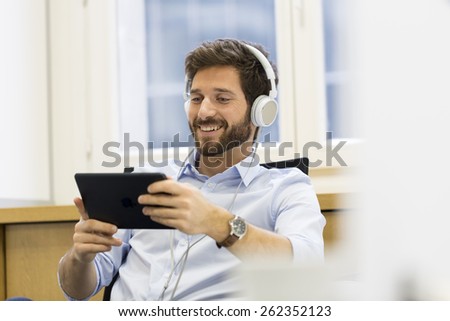 Man in office withe tablet pc and headphones listen music