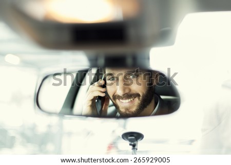 Cheerful man on mobile phone in the car. Reflection in the mirror