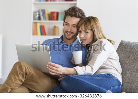 Young couple surfing on internet with laptop. Modern white apartment in background