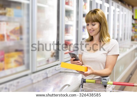 Cheerful young woman texting on mobile phone in supermarket