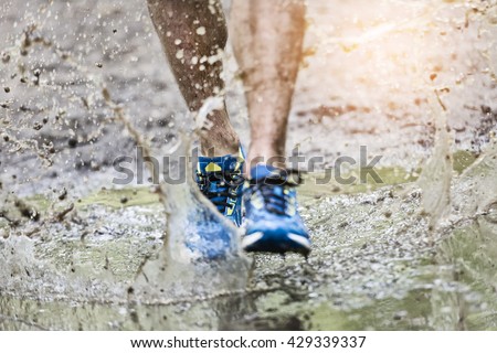Trail runner man walking in a puddle, splashing his shoes. Cross country trail