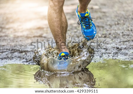 Running man walking in a puddle, splashing his shoes. Cross country trail. Freeze action