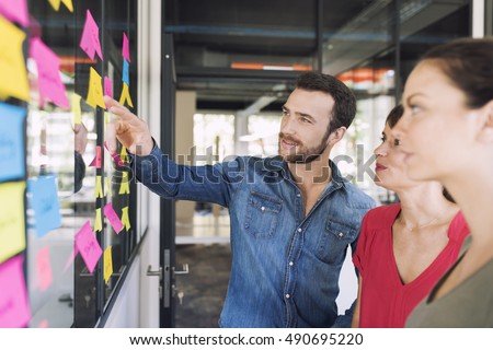Three businesspeople discussing and planning concept. Front of glass wall marker and stickers. Startup office.