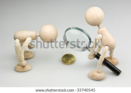 Small change. Two Wooden doll, looking to a 50-Cent-coin trough a magnifier