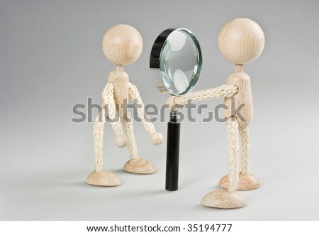 Identity check, security check. A wooden doll is looking to another trough a magnifier