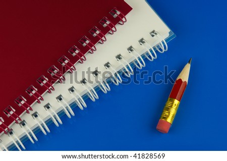 Very short red pencil and two memo pads on blue desk
