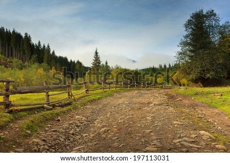 Autumn landscape in a mountain valley: road and wooden fence
