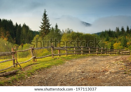 Autumn landscape in a mountain valley: road and wooden fence