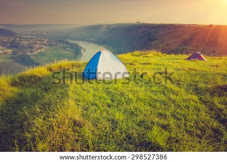 Tourist tent on green meadow at sunrise. Camping background. Freedom concept. Filtered image:cross processed vintage effect.