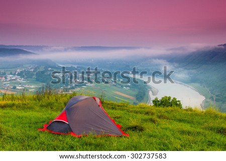 Tourist tent on green meadow at dawn. Camping background. Freedom concept.