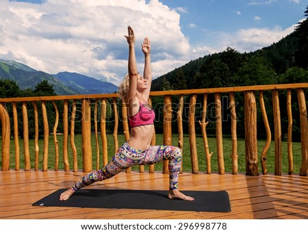 Woman doing yoga over mountains, green field and blue sky background