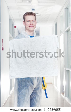 Man cleaning office wearing protective overalls, holding a mop towards camera, room for text