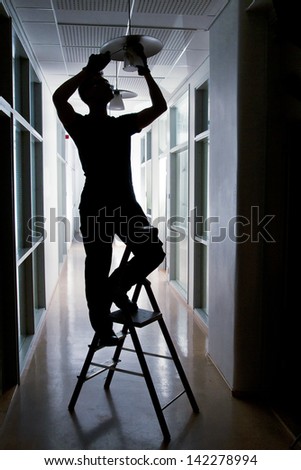 Silhouette of a janitor repairing broken lamp in corridor