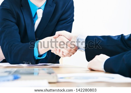 Two businessman shake hands above conference room table