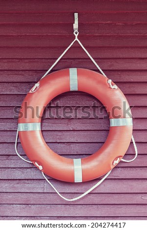 Orange life-buoy hanging on red wooden wall