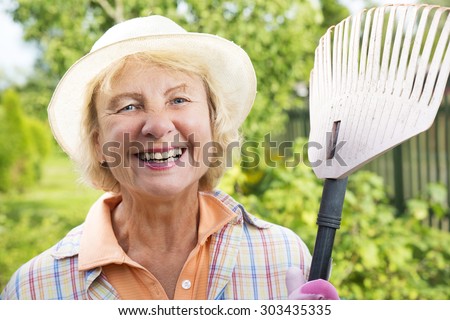 Portrait of a laughing senior woman holding rake in the backyard garden