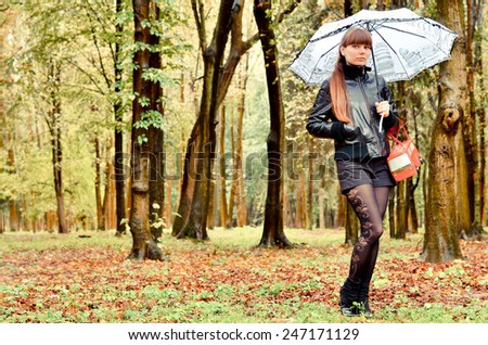 Beauty woman posing in the rain holding an umbrella in park and wearing a  black jacket  with a red bag