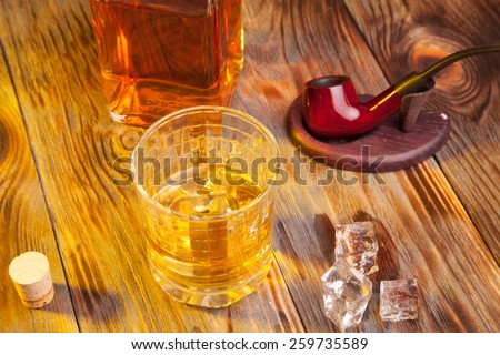 Bottle of whiskey and a glass and tobacco pipe on a wooden table