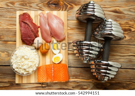 Protein diet, fish, cheese, eggs, meat, chicken and dumbbells on a wooden background