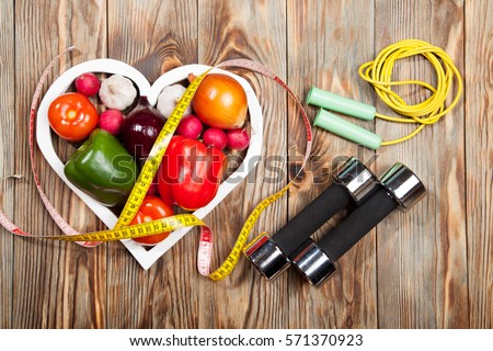 Sport and diet. Vegetables, dumbbells and centimeter. Peppers, tomatoes, garlic, onions, and radishes in the heart on rustic background
