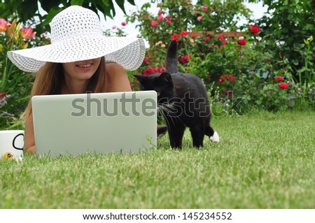 a girl and a cat on the grass watching laptop