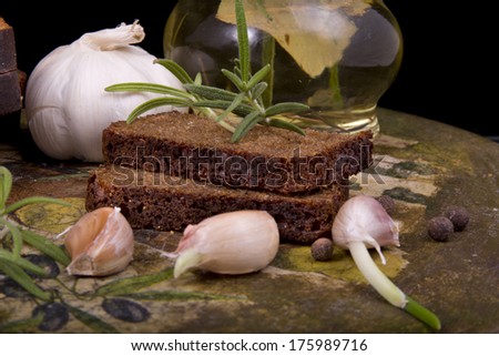 composition of appetizing bottle of olive oil infused with spices, rosemary, garlic, bay leaf and a beautiful decoupage bottles with dark bread on a black background