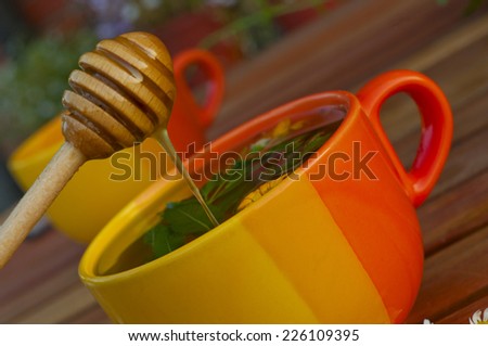 fresh honey flows into the herbal tea in an orange cup