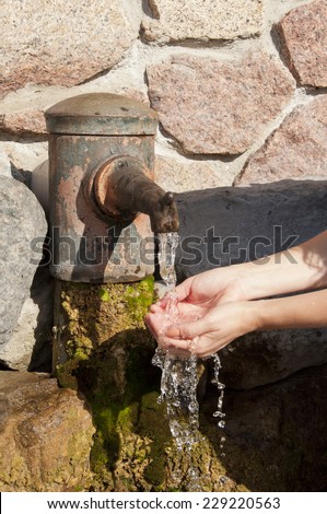female hands under the column with a jet of cold water from the source