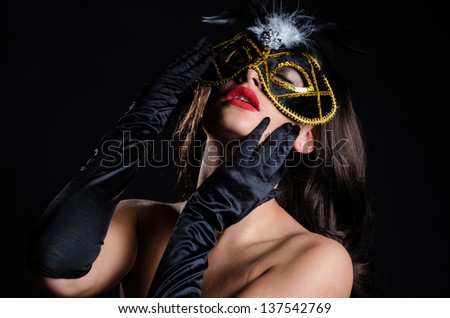 Beautiful, stylish woman with bright red lips, wearing a Venetian style masquerade mask and elbow length opera gloves, while staring intently.