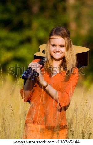 Young hippie girl with a guitar walking in tall grass in orange clothes