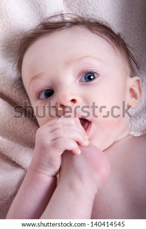 Portrait of a little baby boy with blue eyes naked on a blanket; has his foot in his mouth