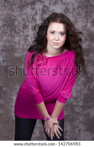 Portrait of a girl with long hair in a pink blouse relies hands on leg