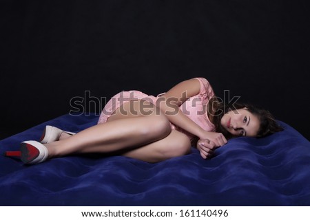 Long-haired young woman in a purple mini dress lying on bed sad