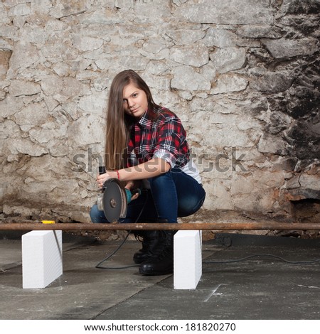 Young long-haired woman cut iron pipe with angle grinder during the repair an old house