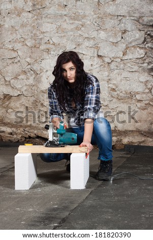 Young long-haired woman with a circular saw cuts wood at repair of an old house
