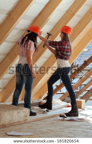 Two young long-haired woman hammered nails into a wooden construction of a new roof on the house