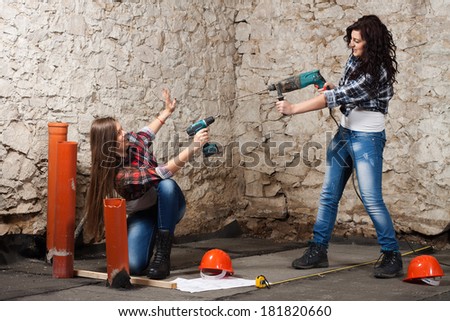 Two young long-haired woman works to repair an old house with an electric drill and cordless screwdriver