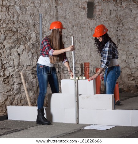 Two young long-haired woman repairing the old house and build a new wall from blocks in accordance with drawing