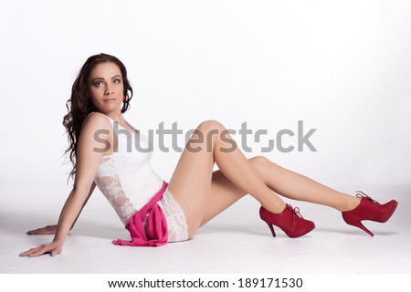 Young woman in a white mini dress, red high heels with a pink scarf sitting on the floor