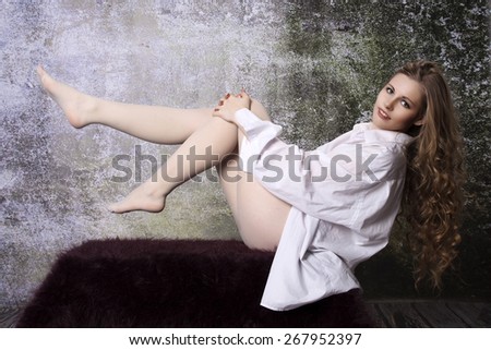 Young long-haired curly blonde woman on the sofa with a hairy blanket in front of an old dilapidated wall