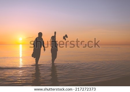 Senior couple throws shoes on the beach