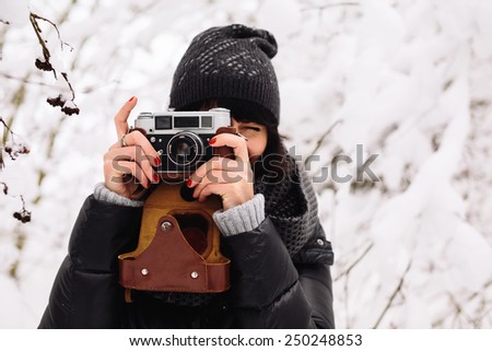 Brunette smiling girl photographed on an old vintage camera in winter forest