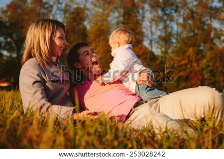 Mom and dad looking at his child and enjoys lying on meadow