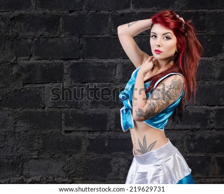 Beautiful tattooed Girl with red hair standing over a grungy dark wall. tattoo pinup dress