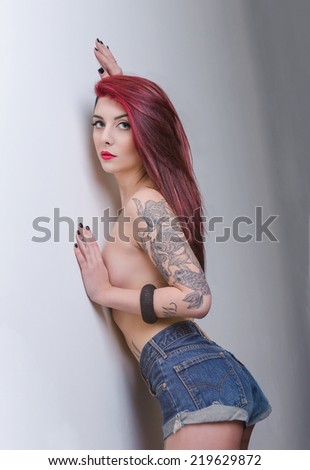 Beautiful tattooed Girl with red hair standing still over a white background. tattoo