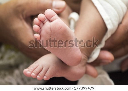 Baby feet with Mom\'s hand on white coverlet