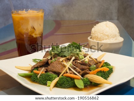 Beef Siam Thai food dish, composed of beef, broccoli, corn, snow peas, and carrots, shown with Thai iced tea and rice