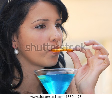 Girl eating a fresh orange fruit from a glass of turquoise blue cocktail